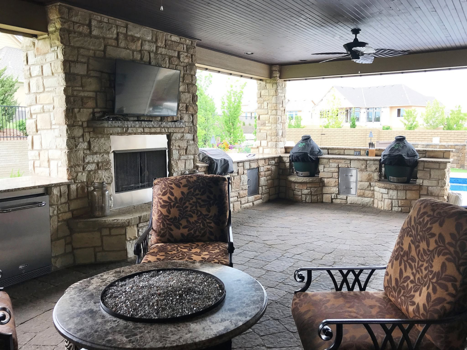 Covered stone patio with fireplace, fire table and outdoor kitchen by TenderCare