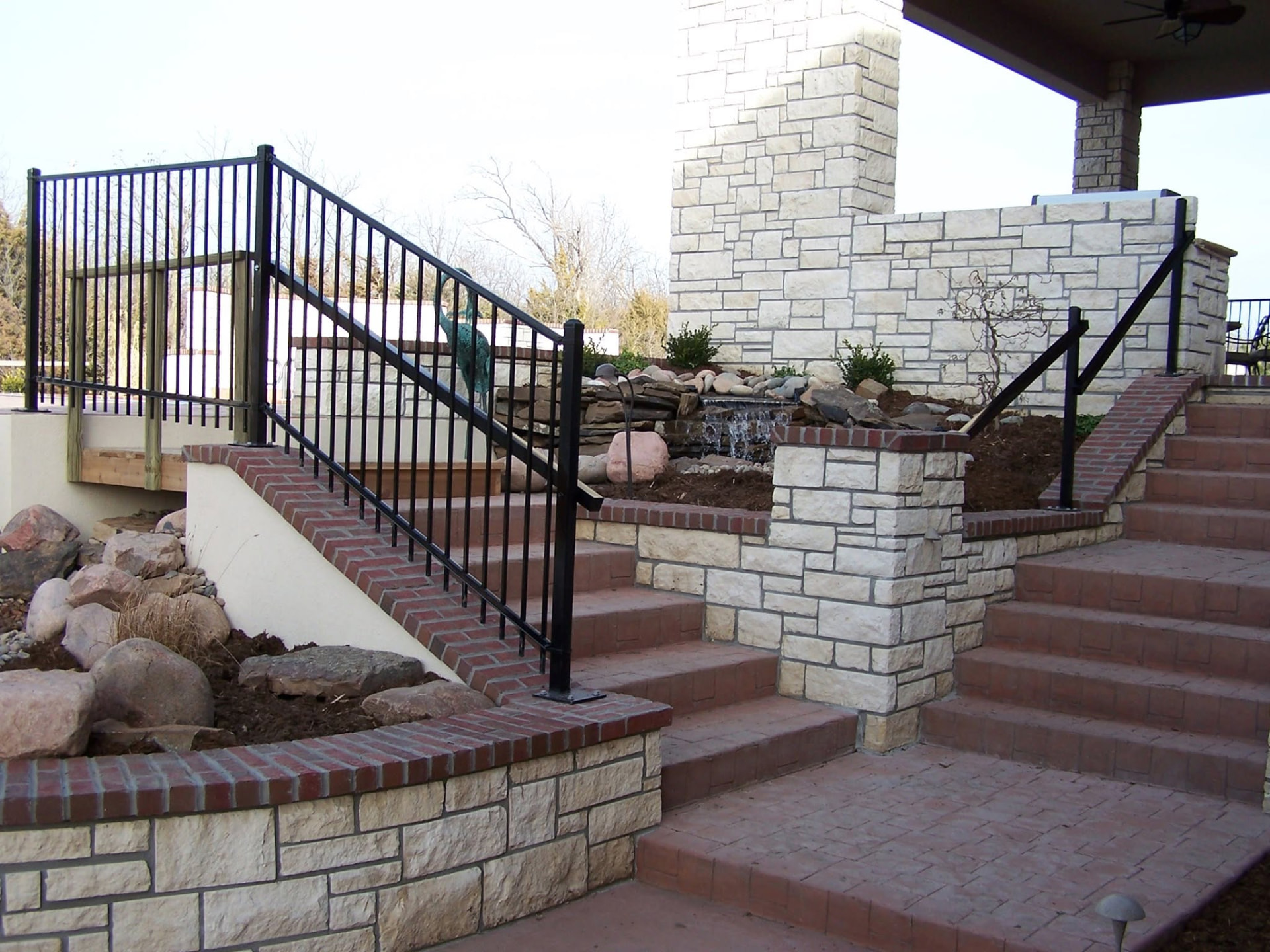 Brick steps and landings with stone retaining walls, a waterfall and an outdoor fireplace — client-supplied TenderCare photograph