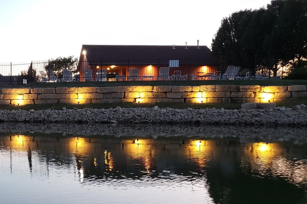 Lit pavilion and water feature at dusk, with uplighting on a stone retaining wall — client-supplied TenderCare photograph